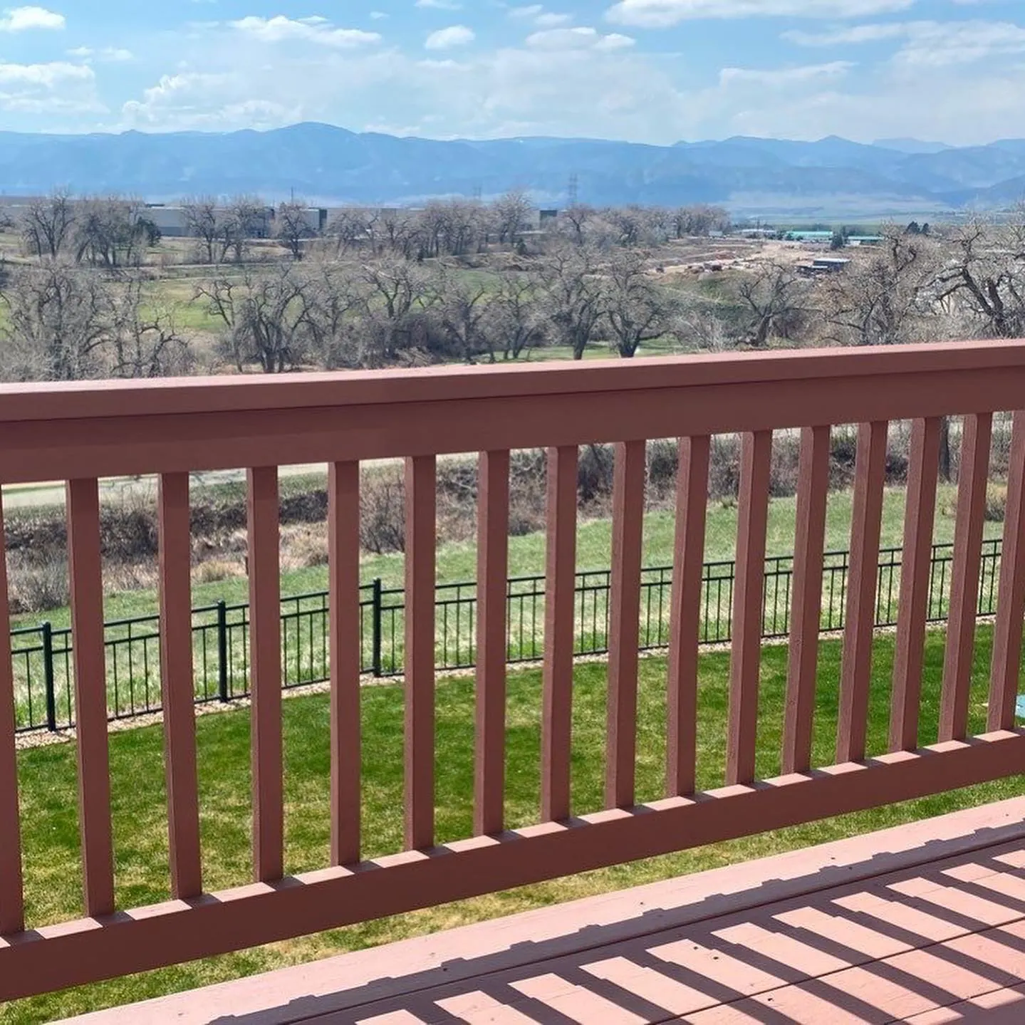 A stained deck railing on a Denver-area home with the Front Range behind it